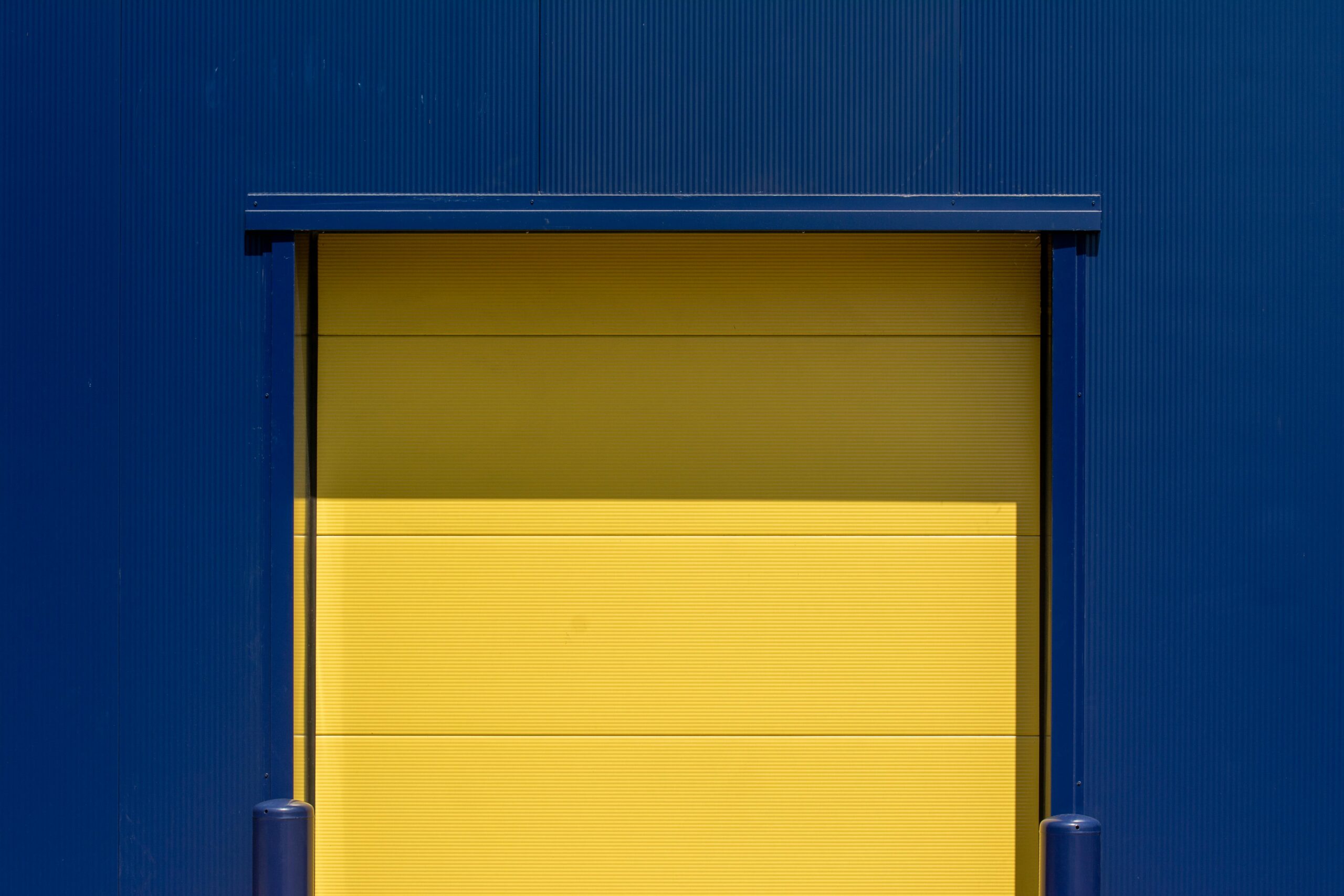 Vibrant yellow industrial door set against a blue metal wall, showcasing modern urban design.